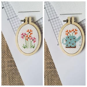 May include: Two embroidery hoop crafts. The first hoop features a cross-stitch design of pink and orange flowers. The second hoop features a cross-stitch design of a blue watering can with orange flowers.