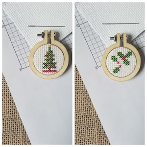 May include: Two small wooden embroidery hoops with cross-stitch designs. The left hoop features a green Christmas tree with red ornaments and a red base. The right hoop features a green holly sprig with red berries.