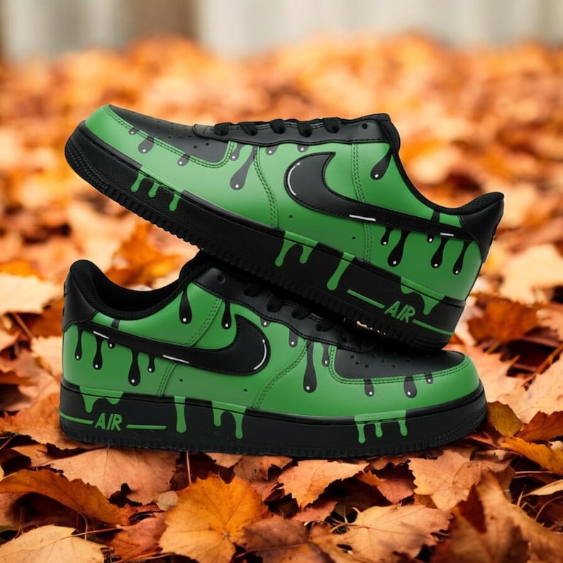 May include: Black and green trainers with a drip design. The trainers have a black swoosh and the word "AIR" on the side. The shoes are set against a backdrop of autumn leaves.