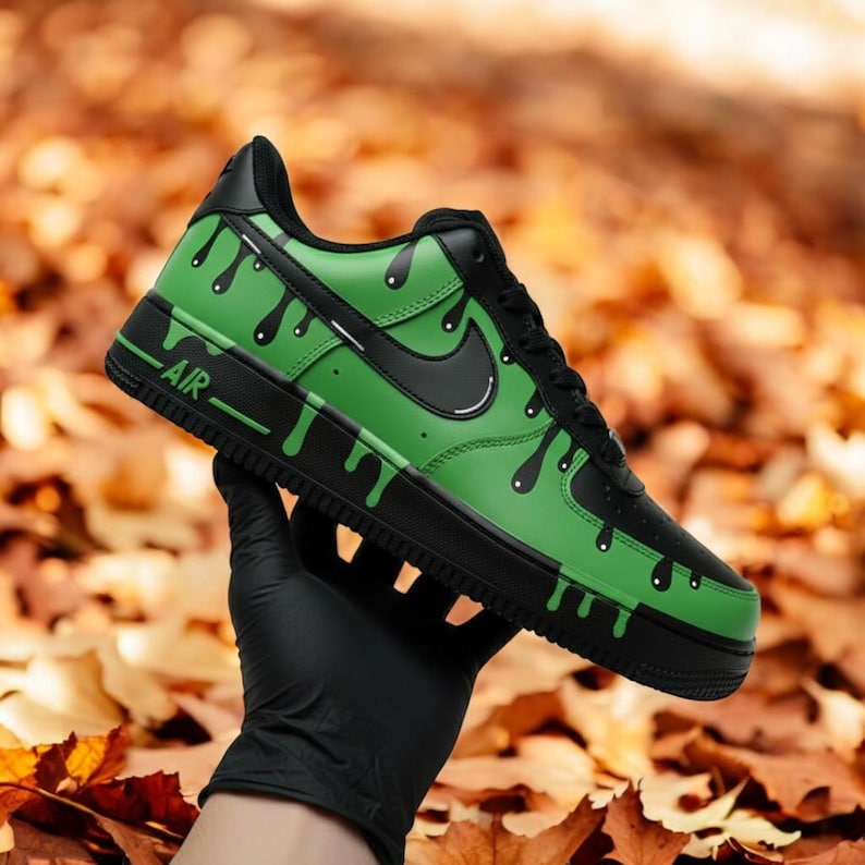 May include: A custom Air Force 1 trainer in black and green. The shoe has a green base with black dripping paint details, a black Nike swoosh, and black accents. The word "AIR" is visible on the side.