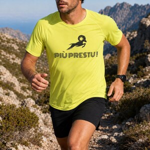 Puede incluir: Una camiseta deportiva de manga corta en color amarillo neón con un gráfico negro de un carnero saltando sobre el texto PIÙ PRESTU! en una fuente sans-serif en negrita. La camiseta tiene cuello redondo, mangas raglán y pantalones cortos negros.