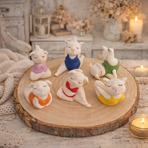 Könnte beinhalten: Eine Sammlung weißer Keramik-Schwein-Figuren in verschiedenen Yoga-Posen, jede mit farbigen Outfits. Die Schweine sind auf einer Holzscheibe angeordnet, mit Kerzen und dekorativen Elementen im Hintergrund.