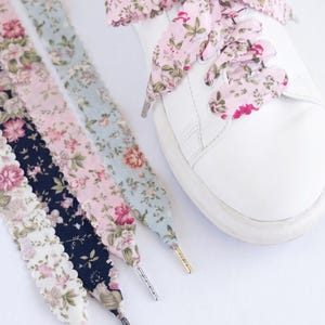 May include: White trainer with floral print shoelaces in pink, blue, and navy. The laces have a scalloped edge and metallic aglets. One shoe is laced with pink floral laces, others are displayed separately.