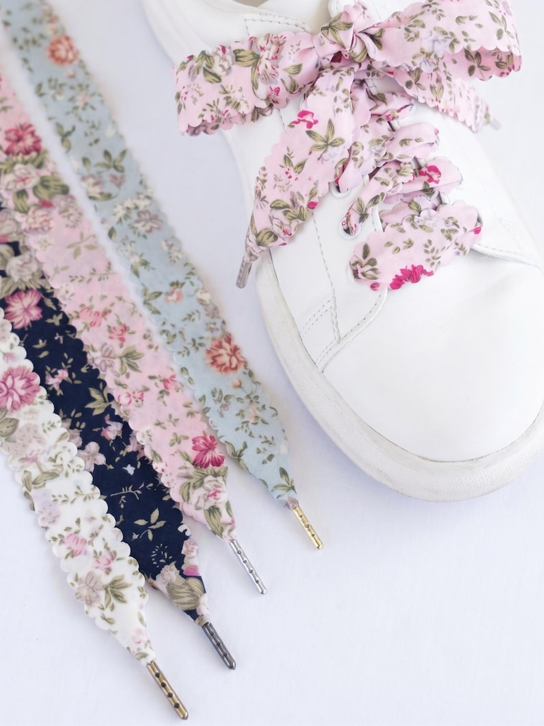 May include: White trainer with floral print shoelaces in pink, blue, and navy. The laces have a scalloped edge and metallic aglets. One shoe is laced with pink floral laces, others are displayed separately.