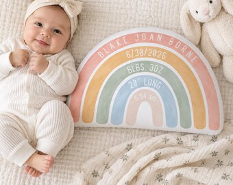 May include: A semi-circular decorative pillow featuring a rainbow design in muted tones of pink, yellow, green, and blue. The pillow is personalized with the text BLAKE JOAN BORNE, 6/30/2026, 6LBS. 3OZ, 20" LONG, and 5:54 am printed in white.