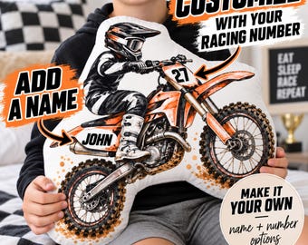 May include: A white throw pillow featuring a graphic illustration of a motocross rider on an orange dirt bike. The design includes the text JOHN, the number 27, and promotional text reading CUSTOMIZE WITH YOUR RACING NUMBER and ADD A NAME.