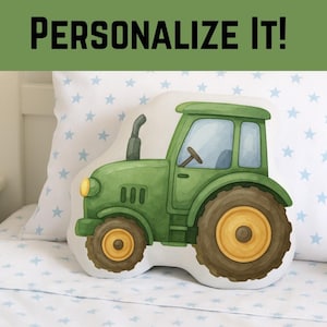 May include: A green tractor-shaped pillow with yellow wheels and a black smokestack. The pillow is on a bed with a white pillow and a blue star pattern. The text "PERSONALIZE It!" is at the top.