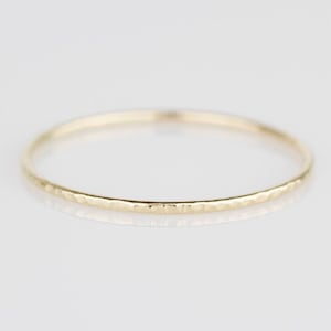 May include: A thin gold hammered ring. The ring is simple and delicate, with a hammered texture that adds a touch of rustic charm.