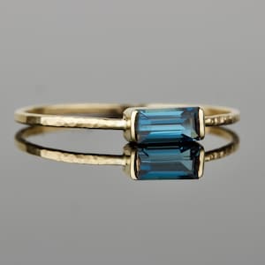 May include: A gold ring with a hammered band and a blue topaz gemstone. The gemstone is a rectangular baguette cut.