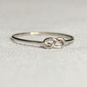 Peut inclure: Une bague en argent simple avec un motif de nœud. La bague est fine et délicate, et le nœud est un symbole classique d'amour et d'éternité.