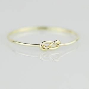 May include: A simple gold ring with a knot design. The ring is thin and delicate, and the knot is a classic symbol of love and eternity.