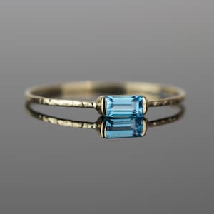 May include: A delicate gold ring with a hammered band and a single, rectangular blue topaz gemstone.