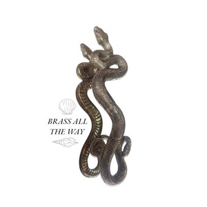 Pu&ograve; includere: Una scultura in bronzo di due serpenti intrecciati, con la testa rivolta verso l'alto. I serpenti sono dettagliati con squame e hanno una finitura dorata.