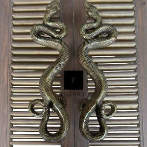 Pu&ograve; includere: Maniglie per porte in ottone antico a forma di serpente. Le maniglie sono montate su una porta in legno con un design a lamelle.
