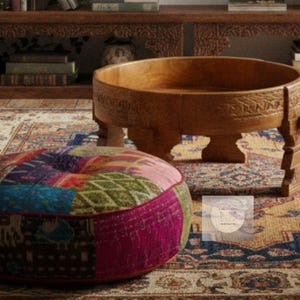 Könnte beinhalten: Ein Holztisch mit geschnitzten Details und ein Patchwork-Pouf. Der Couchtisch ist rund mit einer flachen Schalenform und steht auf kurzen Beinen. Der Pouf besteht aus bunten Stoffflicken.
