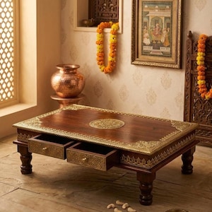 May include: A rectangular wooden coffee table featuring dark brown wood, four sturdy turned legs, and two pull-out drawers. The table surface and drawer fronts are adorned with intricate gold-colored metal filigree detailing and a central medallion.