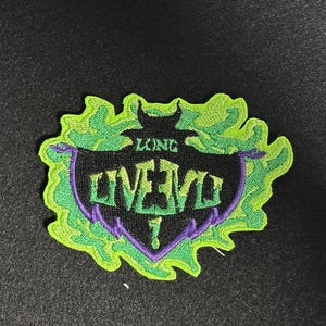 May include: Embroidered patch with the words "LONG LIVE EVIL" in a stylized font. The patch features a black banner with purple accents, surrounded by a green, flame-like border. The patch is on a black background.