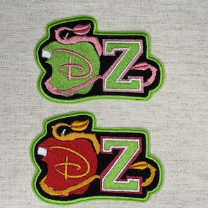 May include: Two embroidered patches featuring a stylized apple shape next to the letter Z. The top patch has a green apple with pink vines and a pink letter Z. The bottom patch has a red apple with gold vines and a green letter Z.