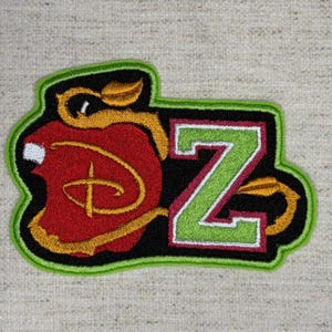 May include: An embroidered patch featuring a red apple shape with a gold outline and a gold leaf, overlaid with a gold stylized letter D. Next to the apple is a large green letter Z with a white and red border, all on a black background.