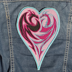May include: A heart-shaped patch with two dragons intertwined. The dragons are pink and black, with blue outlines. The patch is sewn onto a denim jacket.