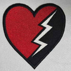 May include: A red heart-shaped patch with a black lightning bolt splitting it in half. The lightning bolt is white.