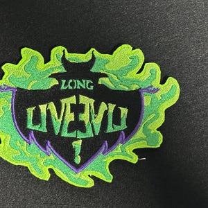 May include: Embroidered patch with a black shield design, featuring the words "LONG LIVE EVIL" in purple and white. The shield is outlined in purple and surrounded by a green, flame-like design. The patch is on a black background.