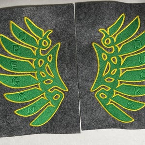 Op de afbeelding: Twee geborduurde groene en gele patches met de tekst "Oregon Ducks" erop.