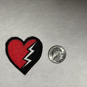 May include: Red and black embroidered iron-on patch of a broken heart with a lightning bolt in the middle.