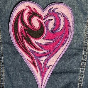 May include: A pink heart-shaped patch with two dragons intertwined. The dragons are black and pink with green eyes. The patch is embroidered with detailed designs.