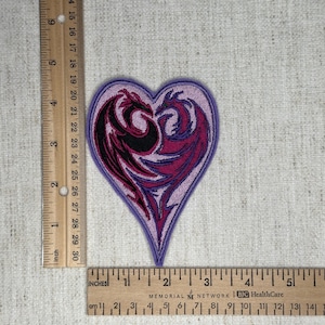 May include: Heart-shaped embroidered patch featuring two stylized dragons in black and shades of pink and purple. The patch is approximately 3 inches wide and 3 inches tall.