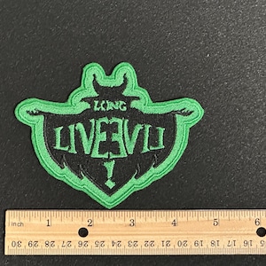 May include: A green and black embroidered patch with the text "LONG LIVE EVIL!" in a shield shape. The patch is approximately 3 inches wide and 3 inches tall.