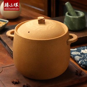 以下が含まれることがあります： 蓋と2つの取っ手が付いた、タン色のセラミック製の調理鍋。 蓋には小さなノブと装飾的な模様があります。 鍋は木製の表面に置かれています。 左上隅に「ZHENSANHUAN」の文字が見えます。