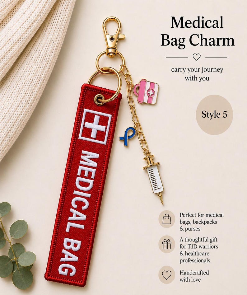 May include: A red rectangular fabric bag tag with white embroidered text reading MEDICAL BAG and a white cross symbol. It features a gold-tone metal lobster clasp, a chain, and three charms: a pink medical kit, a blue ribbon, and a white syringe.