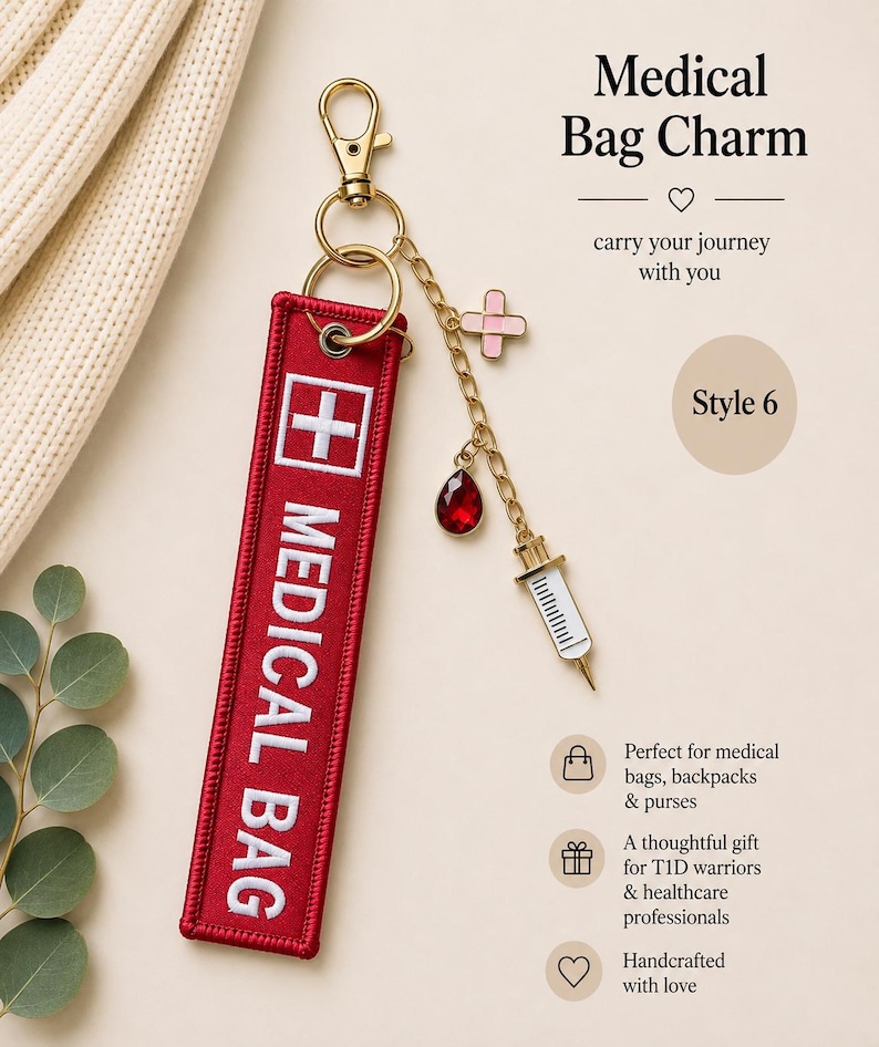 May include: A red fabric keychain tag with white embroidered text reading MEDICAL BAG and a white cross symbol. It features a gold-tone lobster clasp and a gold chain with three charms: a pink bandage, a red teardrop gem, and a white syringe.