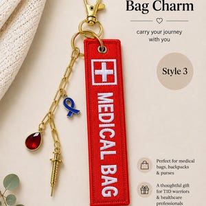 May include: A red rectangular fabric bag charm with white embroidered text reading MEDICAL BAG and a white cross symbol. It features a gold-tone lobster clasp, a gold chain, a blue ribbon charm, a gold syringe charm, and a red teardrop gem.