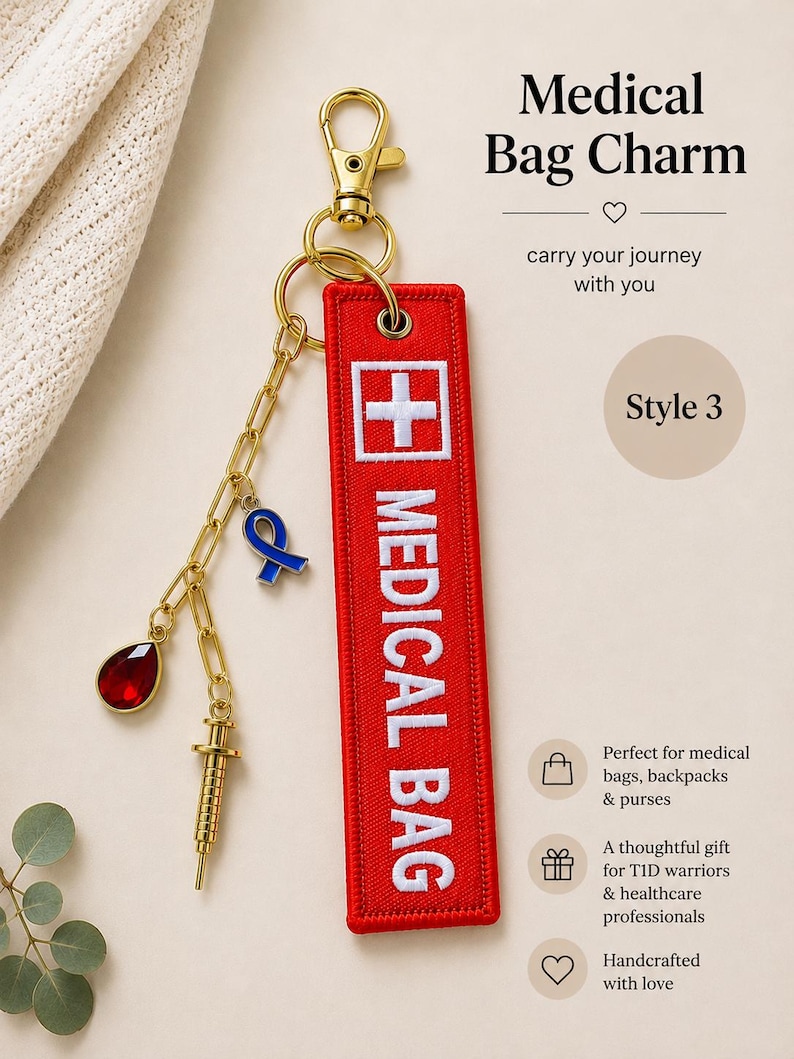 May include: A red rectangular fabric bag charm with white embroidered text reading MEDICAL BAG and a white cross symbol. It features a gold-tone lobster clasp, a gold chain, a blue ribbon charm, a gold syringe charm, and a red teardrop gem.