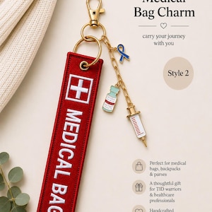 May include: A red rectangular fabric bag charm with white embroidered text reading MEDICAL BAG and a white cross symbol. It features a gold-tone lobster clasp, a split ring, and a gold chain with three enamel charms: a blue ribbon, a vial, and a syringe.