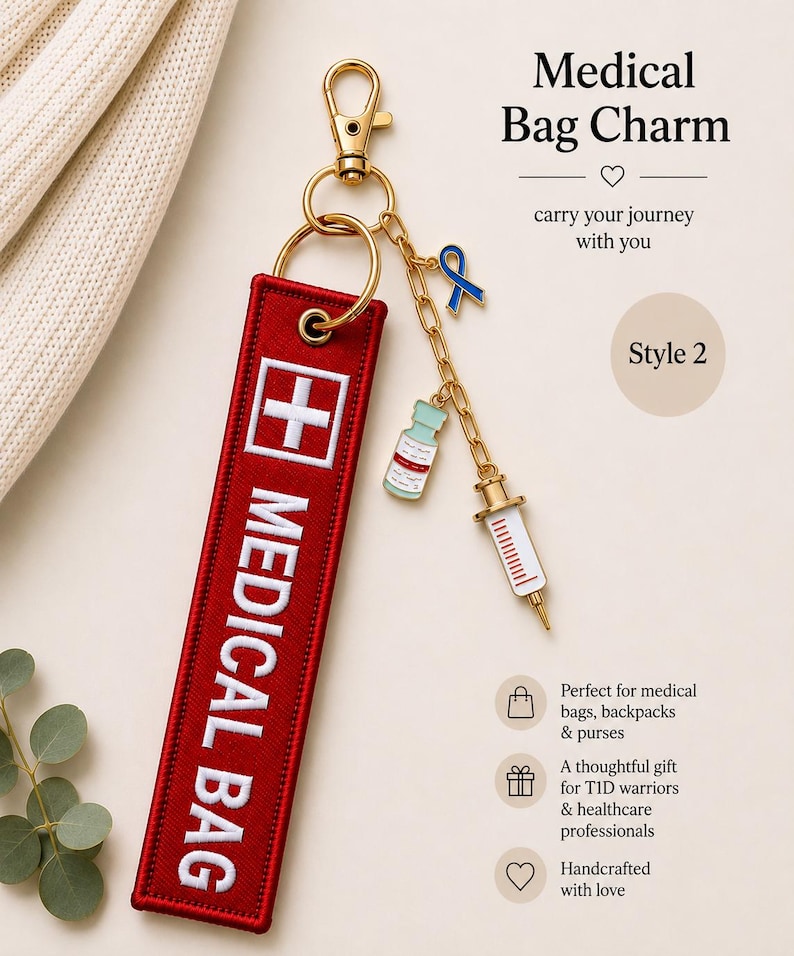 May include: A red rectangular fabric bag charm with white embroidered text reading MEDICAL BAG and a white cross symbol. It features a gold-tone lobster clasp, a split ring, and a gold chain with three enamel charms: a blue ribbon, a vial, and a syringe.