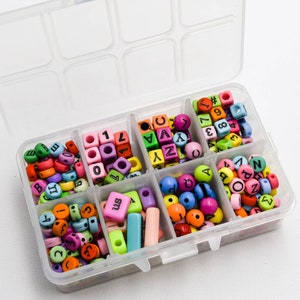 Puede incluir: Una caja de almacenamiento de pl&aacute;stico transparente con ocho compartimentos llenos de cuentas de letras y n&uacute;meros de colores. Las cuentas son de pl&aacute;stico y de varios colores, incluyendo rosa, azul, verde, amarillo y naranja.