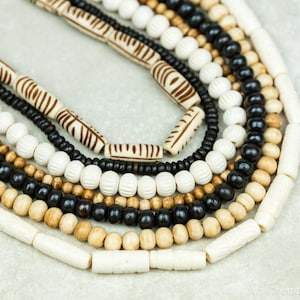 May include: A close-up of a set of wooden bead necklaces. The necklaces are made from different types of wood, including black, white, and brown. The beads are all different shapes and sizes, and some of them have intricate carvings.