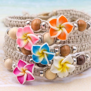 May include: A multi-strand hemp bracelet with wooden and silver beads and five colorful flower charms. The bracelet is woven with a macrame pattern.