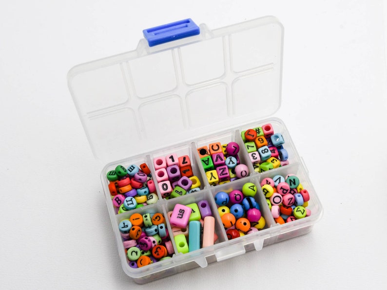 Puede incluir: Una caja de almacenamiento de pl&aacute;stico transparente con ocho compartimentos llenos de cuentas de letras y n&uacute;meros de colores. Las cuentas son de pl&aacute;stico y de varios colores, incluyendo rosa, azul, verde, amarillo y naranja.