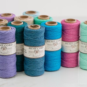 May include: Assortment of 10 spools of hemp cord in various colors, including lavender, teal, turquoise, pink, and mint green. Each spool has a label that reads "Hemp Cord" with a logo and the word "Hemptique".
