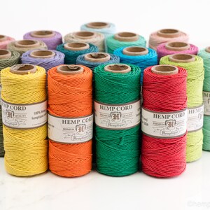 May include: A collection of spools of hemp cord in various colors, including yellow, orange, green, red, and light green. Each spool has a label that reads "Hemptique Hemp Cord Premium Quality 100% Hemp".