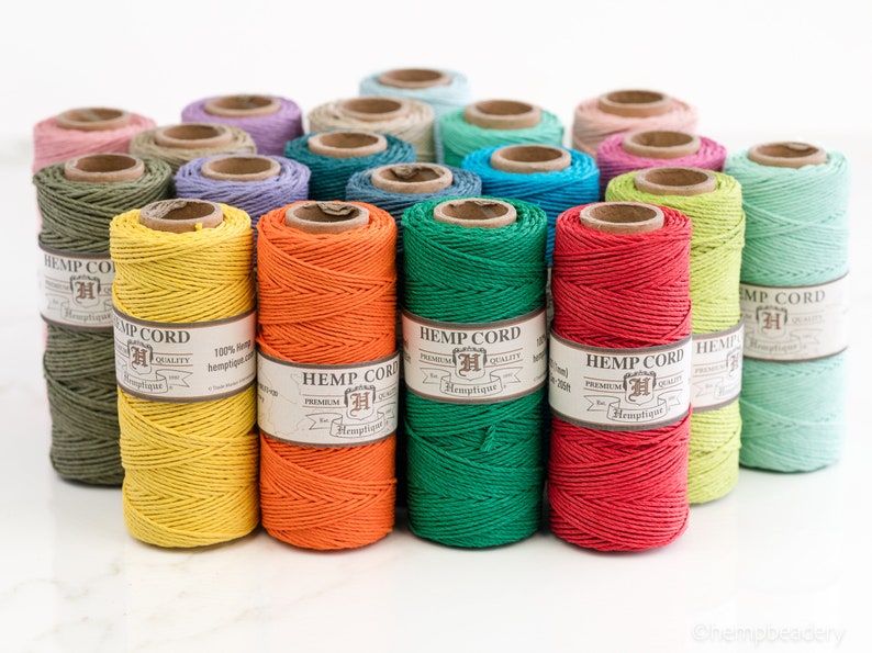 May include: A collection of spools of hemp cord in various colors, including yellow, orange, green, red, and light green. Each spool has a label that reads "Hemptique Hemp Cord Premium Quality 100% Hemp".