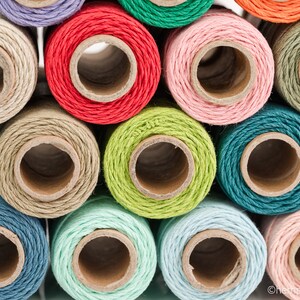 May include: Close-up of spools of colorful twine, including shades of green, blue, red, pink, and beige. The twine is wound around cardboard spools.