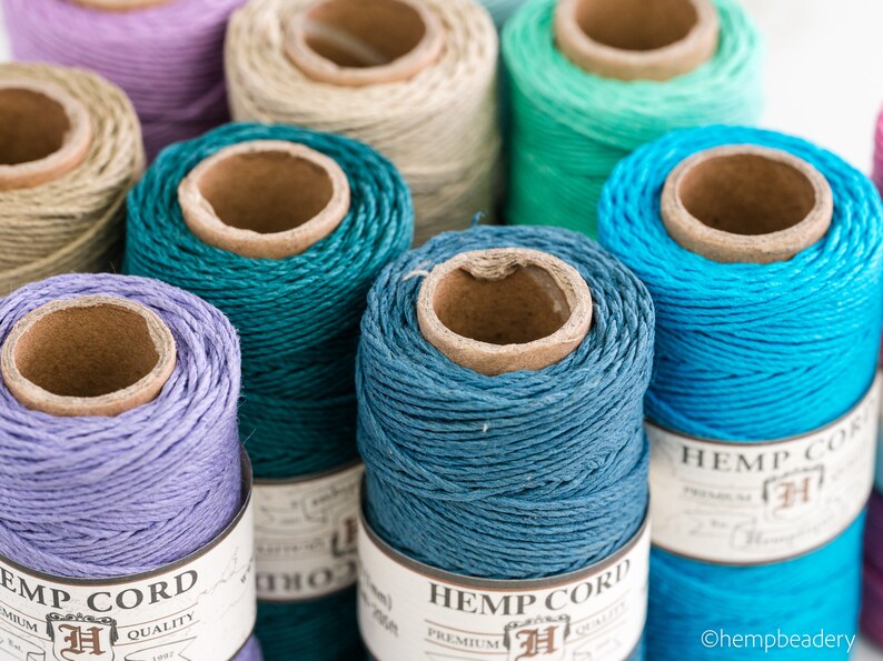 May include: Close-up of spools of hemp cord in various colors, including teal, blue, lavender, and natural. The spools are labeled "Hemp Cord" with a logo and the text "Premium Quality".