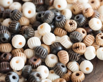 May include: A close-up of a collection of wooden beads in various shades of brown, white, and black. The beads have a textured, grooved surface and are arranged in a random pattern.