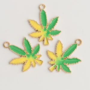 May include: Three gold-toned metal charms in the shape of cannabis leaves. Each leaf is divided into green and yellow sections with a gold outline and a small loop for attaching to jewelry or other crafts.