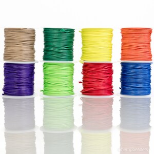 May include: Eight spools of waxed cord in various colors, including natural, green, yellow, orange, purple, lime green, red, and blue. The spools are arranged in a row on a white background.